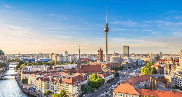 Aerial view of Berlin with the TV Tower rising above red-roofed buildings under a clear blue evening sky