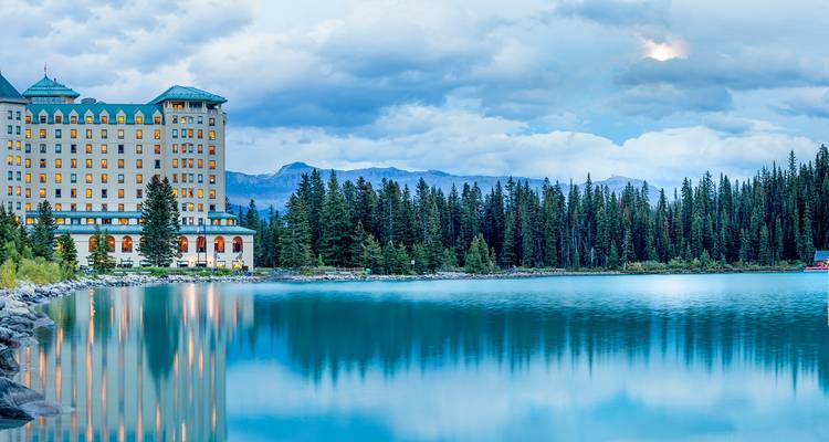 Luxury lakeside hotel reflected in the calm turquoise waters of Lake Louise with forest and distant peaks