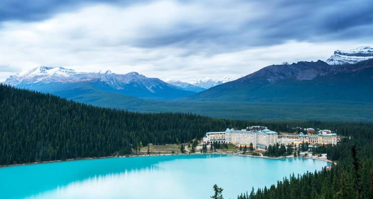 Turquoise Lake Louise bordered by dense pine forest and grand chateau beneath snow-dusted peaks.