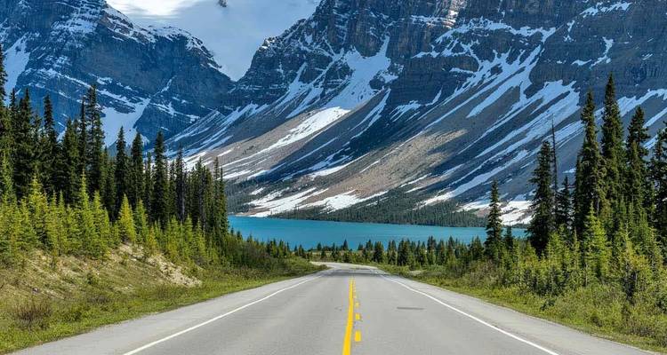 Openweg die leidt naar rotsachtige, sneeuw doorstreepte bergen en het türkooise meer van de Canadese Rockies