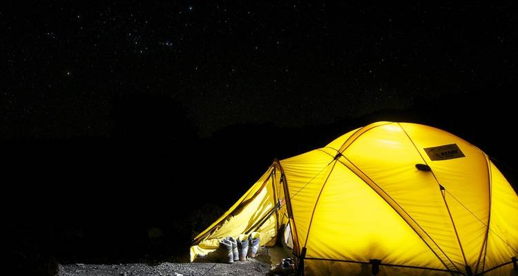 Een helder verlichte gele tent onder een heldere sterrenhemel.