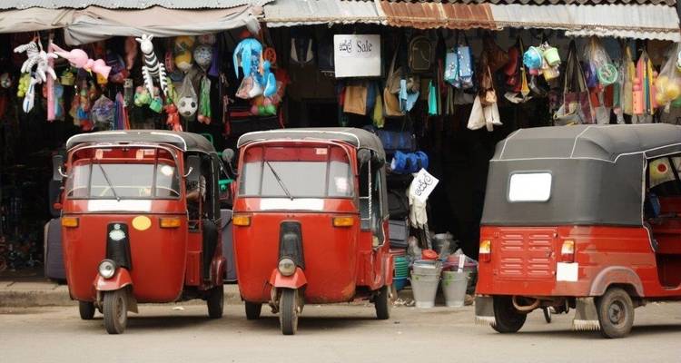 Trois tuk-tuks rouges garés devant un magasin de rue coloré.