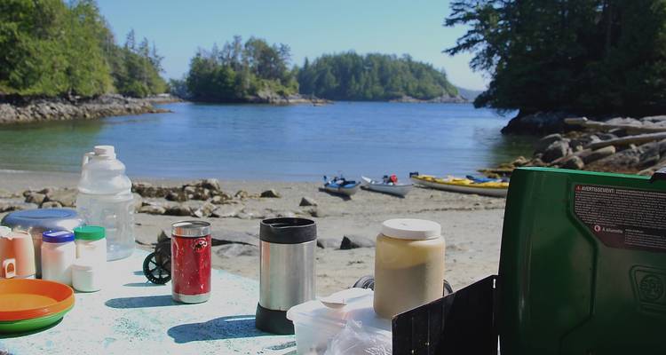 Camping supplies on a beach with kayaks in the background.