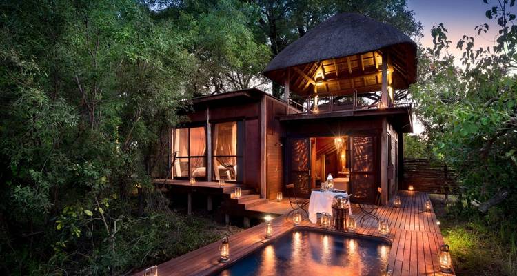 Eine luxuriöse Holzhütte im Wald mit Pool und stimmungsvoller Beleuchtung.