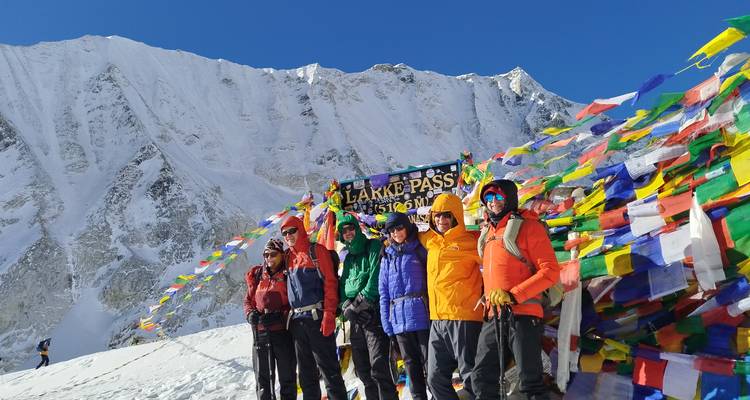 Trekistas en chaquetas coloridas posan junto al letrero del Paso Larke con el telón de fondo nevado del Himalaya