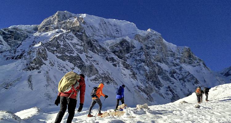 Fila de alpinistas con mochilas ascendiendo una cresta nevada hacia una cumbre escarpada