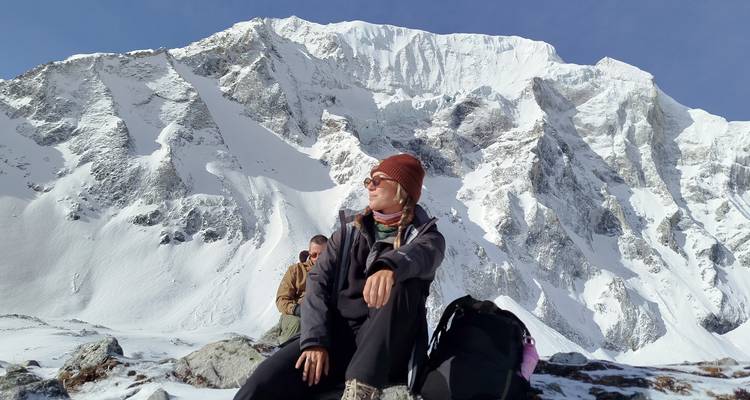 Excursionista descansando en terreno rocoso con la inmensa cara cubierta de nieve del Manaslu de fondo