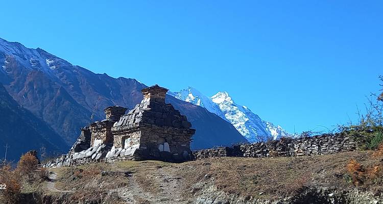 Stone structures on a mountain path with distant snowy peaks.