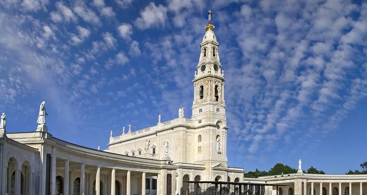 Basiliek van Fátima met colonnes en standbeelden onder een lucht vol patronen van wolken