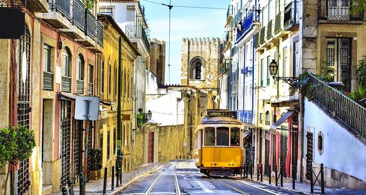 Klassieke gele tram die een smal kinderkopjestraat in Lisbons historische wijk Alfama op rijdt