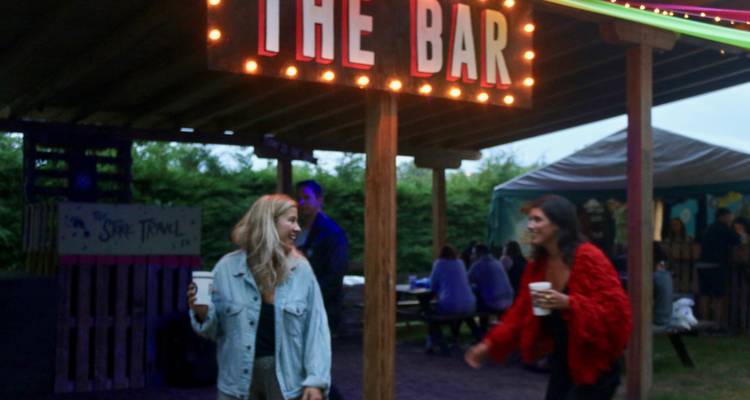Deux femmes sous un panneau de bar tenant des boissons