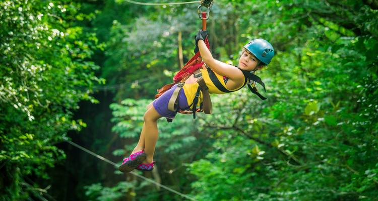 Een jonge avonturier glijdt in een helm en tuigje door het weelderige regenwoud op een zip-line.