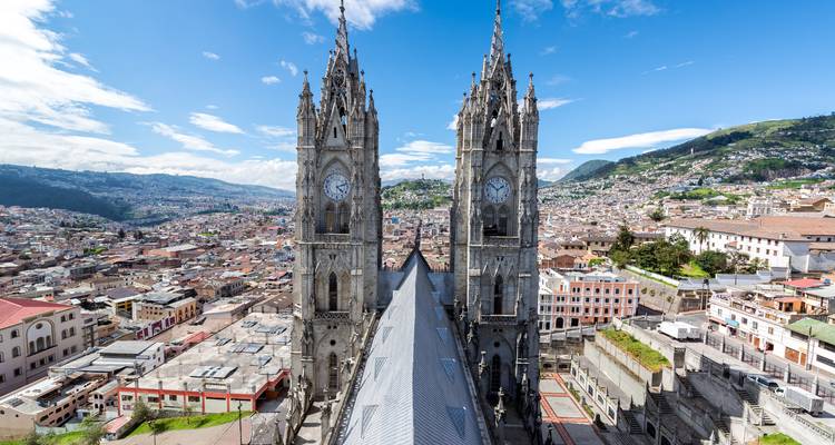 Aerial view of the Basílica del Voto Nacional in Quito, Ecuador, with cityscape and mountains in the background.