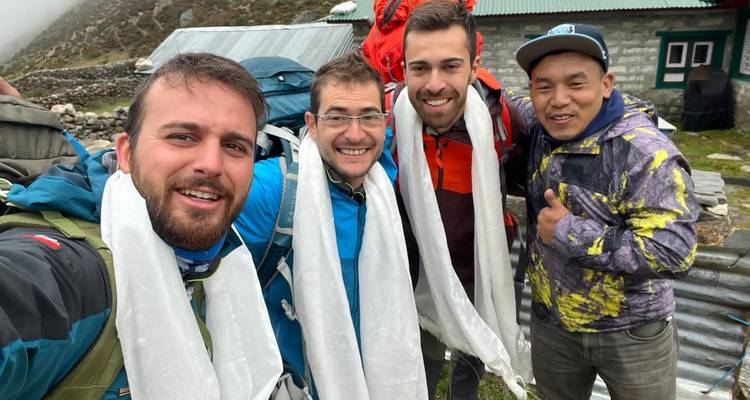 Groupe de personnes souriantes portant des écharpes, avec un bâtiment en arrière-plan.