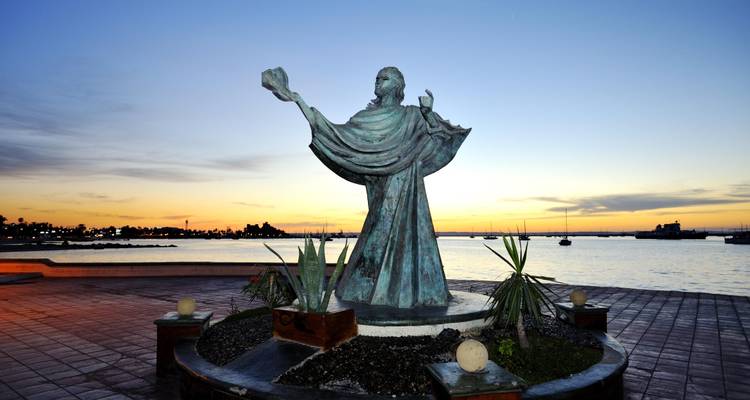 Estatua de una figura al atardecer junto al malecón.