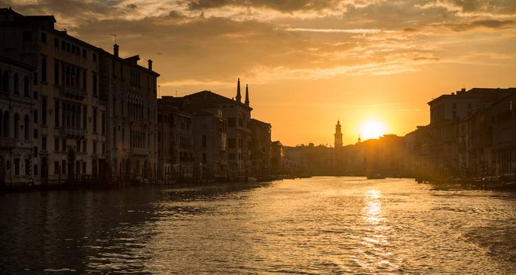 Le soleil doré se couchant sur le Grand Canal créant des silhouettes de bâtiments vénitiens