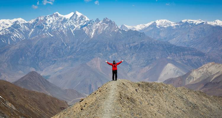 Solo wandelaar in rood jasje staat triomfantelijk op een bergrug met uitzicht op de met sneeuw bedekte Himalaya.
