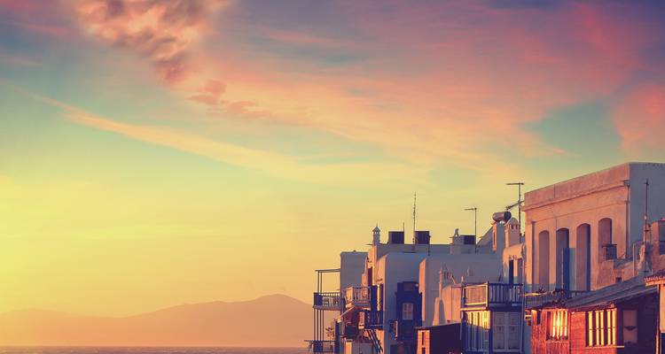Coastal town bathed in warm pastel evening light with mountains faintly visible in distance.