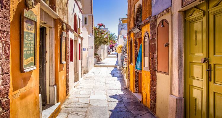 Sunlit Mediterranean alley with colorful doors, stone walls and bright bougainvillea.