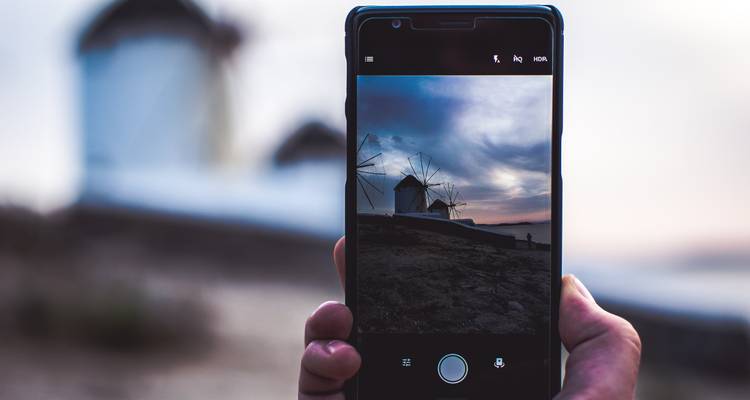 A smartphone held up framing iconic white windmills against a dusky sky.