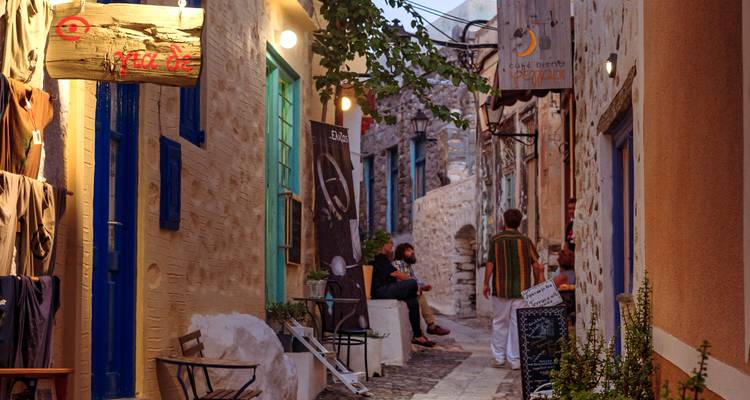 A narrow alley lined with rustic stone buildings and warm lights, people relaxing at a café.