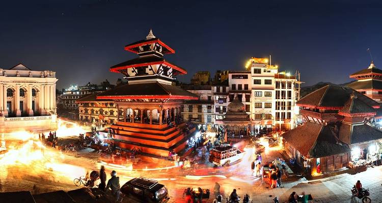 Una plaza vibrante por la noche con templos y actividades bulliciosas.