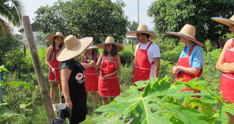 Group of people in red aprons and straw hats in a garden setting.