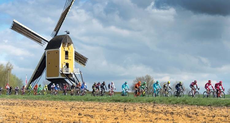 Fietsers die voorbij een windmolen rijden in een landelijke omgeving.