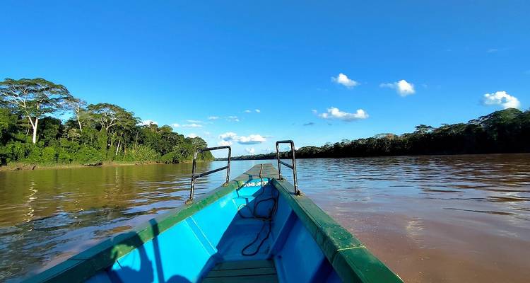 Long canot motorisé naviguant une rivière boueuse bordée par la dense forêt tropicale amazonienne.