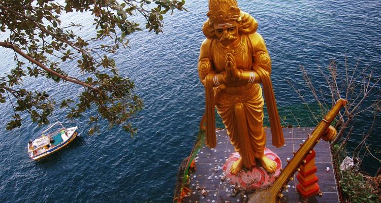 Große goldene Statue mit Blick auf das Meer und einem kleinen Boot in der Nähe.