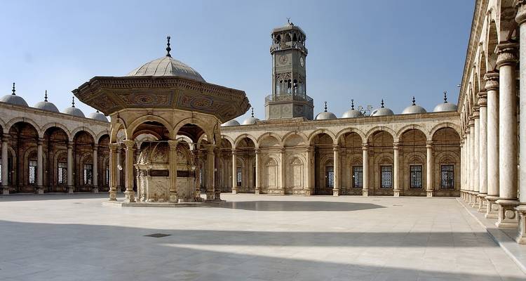 A vast courtyard with an ornate fountain and columns under a clear sky.