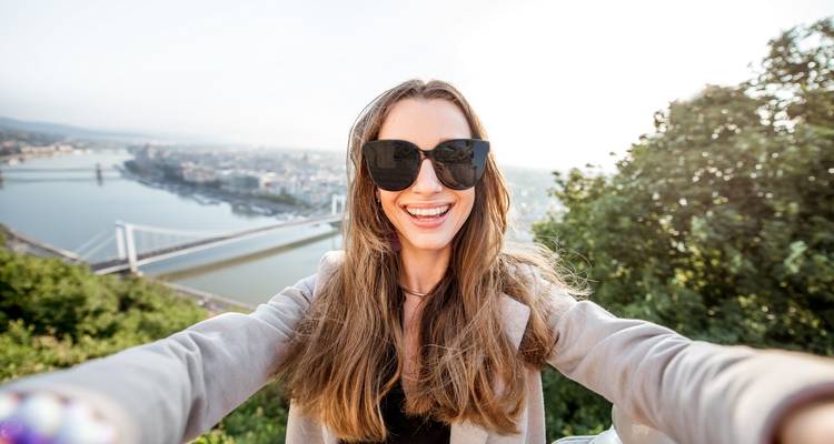 Vrouw die een selfie neemt met een stadsgezicht en brug op de achtergrond