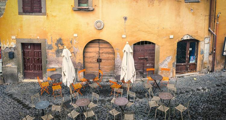Patio de adoquines vacío con sillas naranjas y paredes amarillas gastadas en un barrio italiano antiguo.