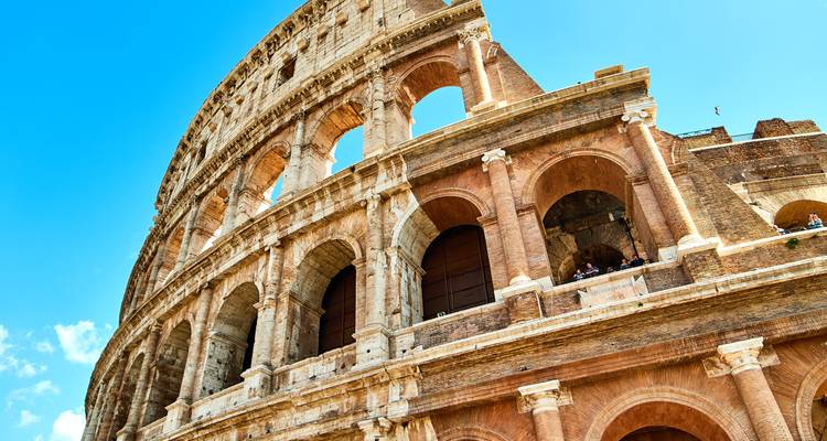 Perspectiva dramática y de cerca del Coliseo de Roma bajo un cielo azul radiante.