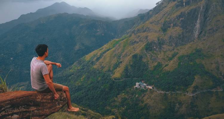Persoon die op een klif zit met uitzicht op bergen.