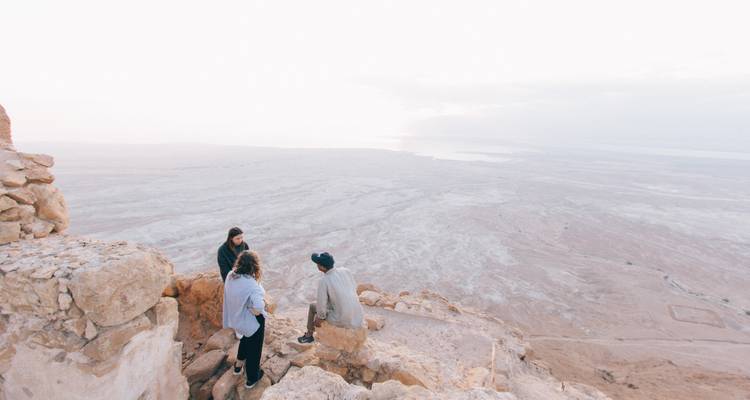 Trois personnes assises sur une falaise rocheuse surplombant un vaste paysage désertique.