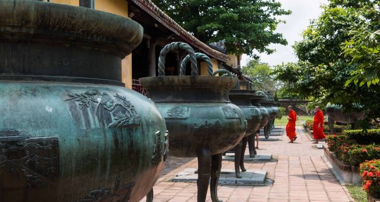 Monks walking past giant urns in a temple courtyard.