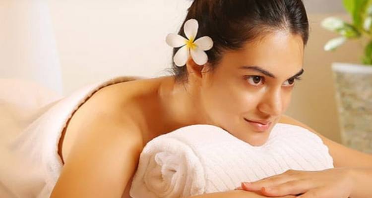 Smiling woman with a plumeria in her hair resting on spa towels, ready for treatment.