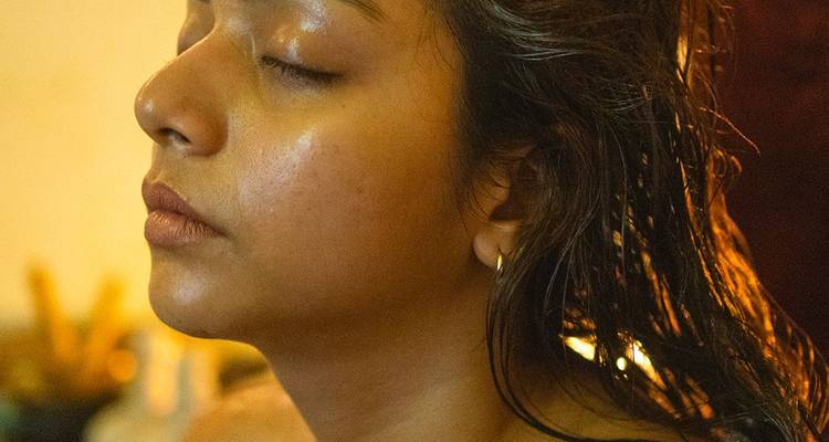Close-up profile of a woman with wet hair receiving an oil head treatment, eyes closed peacefully.