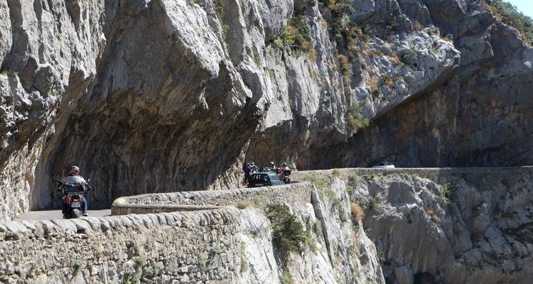 Motorradfahrer, die auf einer in felsige Klippen gehauenen Straße unterwegs sind.
