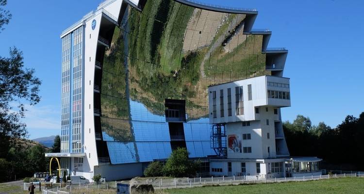 Modernes Solargebäude mit einer verspiegelten Oberfläche, die die Landschaft widerspiegelt.