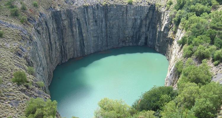 A striking circular turquoise pool enclosed by steep grey rock walls and green scrub.