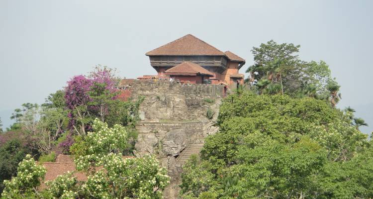 Un edificio histórico en la cima de una colina rodeado de árboles y vegetación.