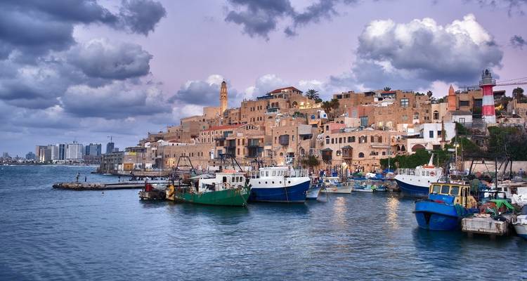 Zeezicht van een historische havenstad met vissersboten en wolken.