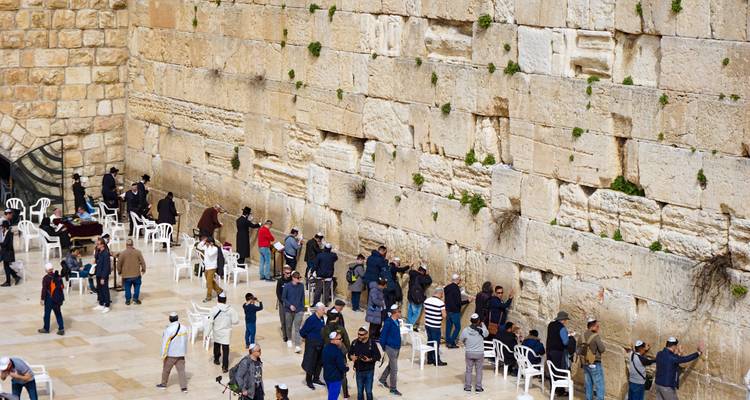 Mensen die bidden bij een historische muur met stoelen in de buurt.