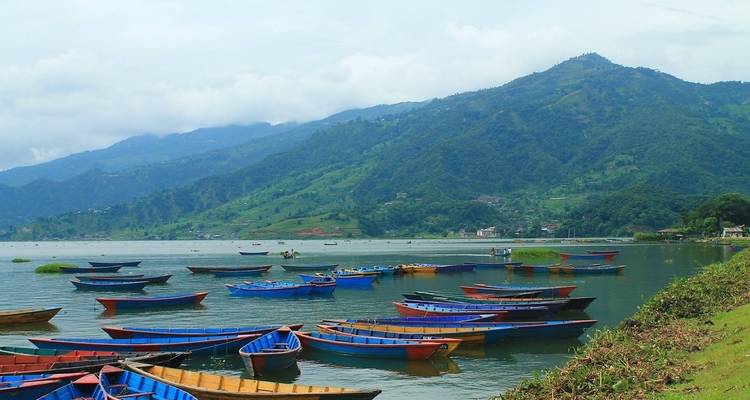Colorful boats docked at a lush, green lakeside with mountains in the background.