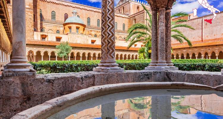 Cour du cloître de la cathédrale de Monreale près de Palerme avec colonnes à motifs, palmiers et toits de tuiles reflétés dans une fontaine.
