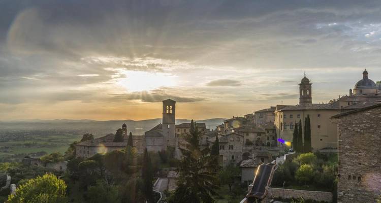 Ciudad medieval de Assisi en la colina bañada por la luz dorada del atardecer con la campiña umbra ondulante más allá