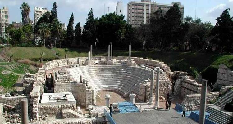 Ruinen des antiken römischen Theaters, umgeben von Bäumen und modernen Gebäuden in Alexandria.