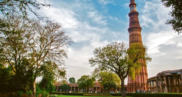Qutub Minar met omringend groen onder een heldere blauwe hemel.